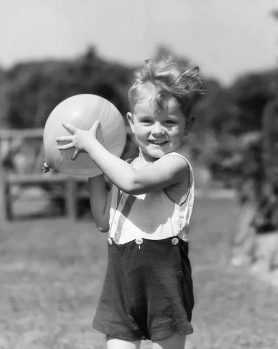 1930s SMILING BOY SUMMER OUTDOOR PLAYING IN BACKYARD LOOKING AT CAMERA READY TO TOSS BALL 