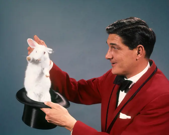  1960s 1970s MAN MAGICIAN WEARING RED SUIT PULLING WHITE RABBIT OUT OF TOP HAT