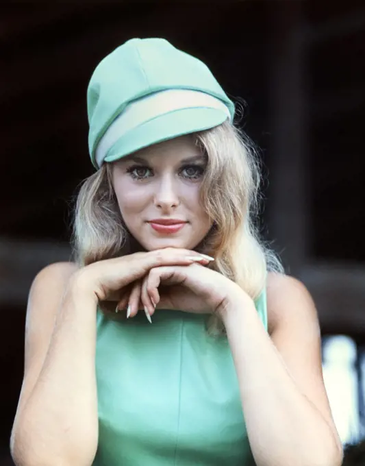 1960s SEXY BLONDE WOMAN PORTRAIT CHIN RESTING ON HANDS TURQUOISE BLUE DRESS & SILLY MOD FASHION CAP HAT