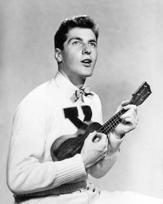 1940s 1950s COLLEGE BOY WEARING X LETTER SWEATER SINGING AND PLAYING UKULELE