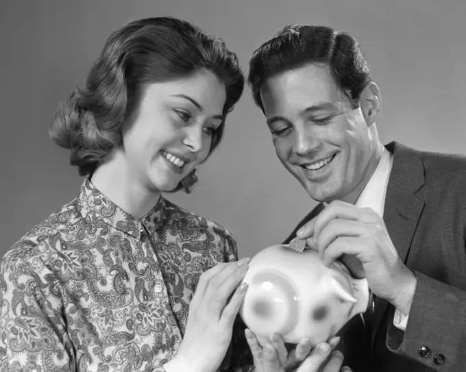 1960s PORTRAIT OF COUPLE PUTTING MONEY INTO PIGGY BANK
