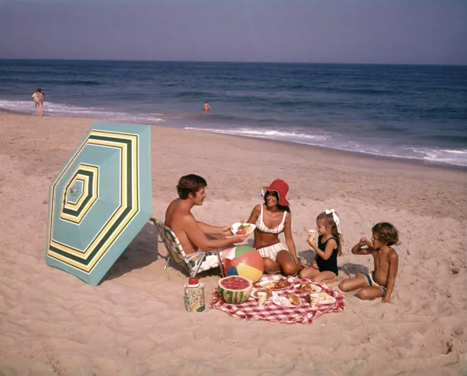 1970s FAMILY EATING PICNIC AT OCEAN BEACH 