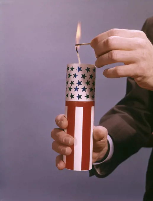 MALE HANDS LIGHTING A GIANT RED WHITE AND BLUE AMERICAN FIRECRACKER