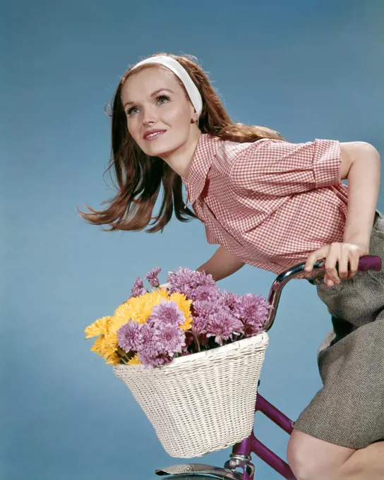 1960s REDHEAD WOMAN RIDING BICYCLE WITH BASKET FULL OF AUTUMN FLOWERS
