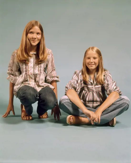1970s TWO TEEN GIRLS SISTERS SMILING WEARING PEASANT SHIRTS BLUE JEANS SITTING AND KNEELING TOGETHER LOOKING AT CAMERA