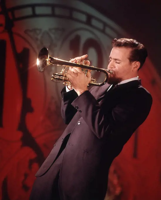 1960s MAN JAZZ MUSICIAN PLAYING TRUMPET NEAR MIDNIGHT NEW YEARS CLOCK FACE IN BACKGROUND