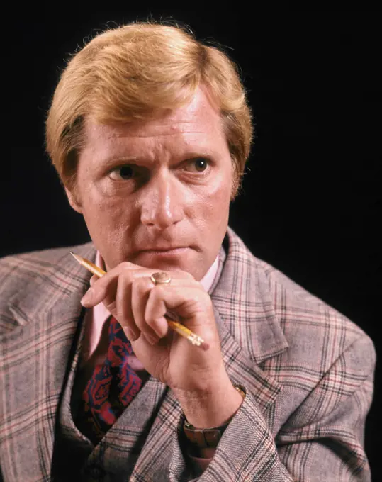 1970s BLOND BUSINESSMAN WITH AMBIGUOUS FACIAL EXPRESSION WEARING THREE PIECE PLAID SUIT HOLDING PENCIL