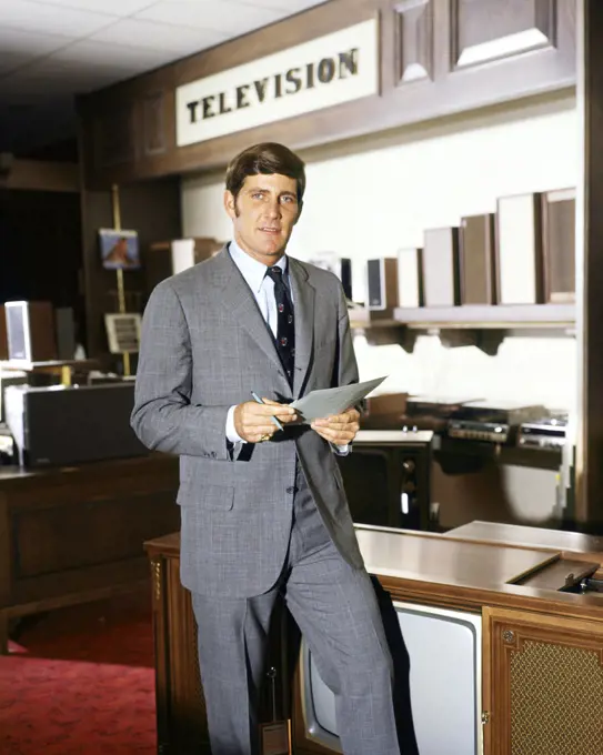 1960s SALESMAN STANDING IN TELEVISION SECTION OF DEPARTMENT STORE LOOKING AT CAMERA 