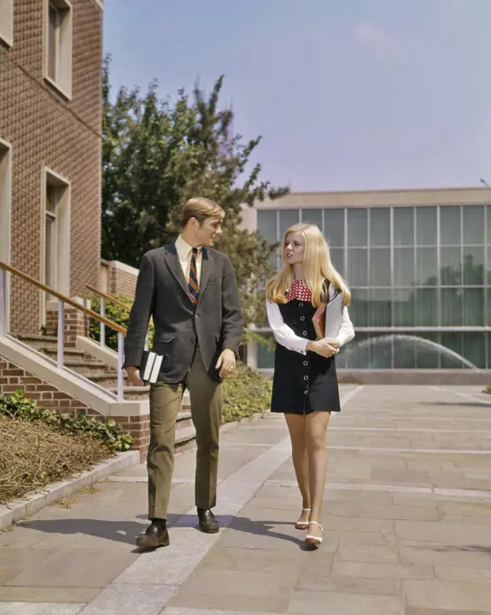 1960s 1970s YOUNG ADULT STUDENT COUPLE WALKING SIDE BY SIDE ON CAMPUS GIRL IN MINIDRESS BOY IN SUIT TIE 