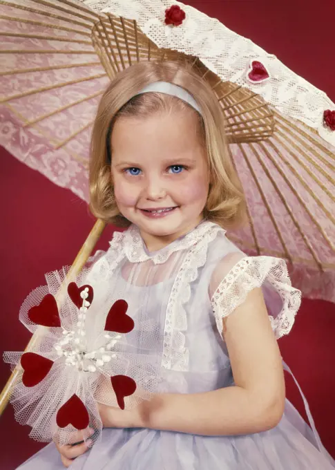 1950s SMILING LITTLE BLOND GIRL LOOKING AT CAMERA WITH VALENTINE BOUQUET OF RED HEARTS AND FLOWERS UNDER LACY PARASOL UMBRELLA