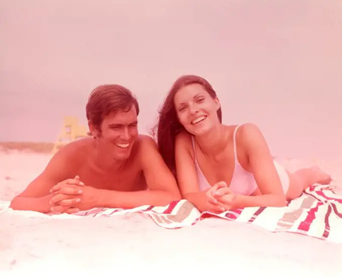 1960S Smiling Young Couple Lying Side By Side Together On Beach Towel
