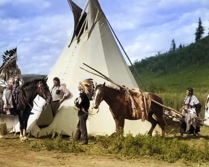 1920s STONEY SIOUX MEN AND WOMEN WITH HORSE PULLING TRAVOIS BY TIPI, ALBERTA, CANADA