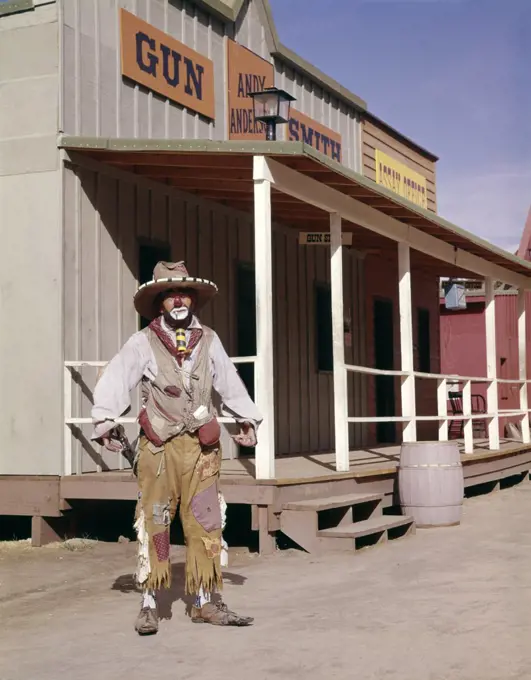 1960S Sad Clown In Cowboy Costume Standing In Street Of Western Frontier Town  