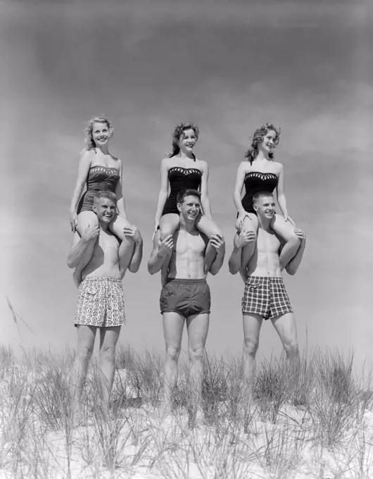 1950S 1960S Three Couples At Beach On Dunes With Women In Identical Bathing Suits Sitting On Men'S Shoulders