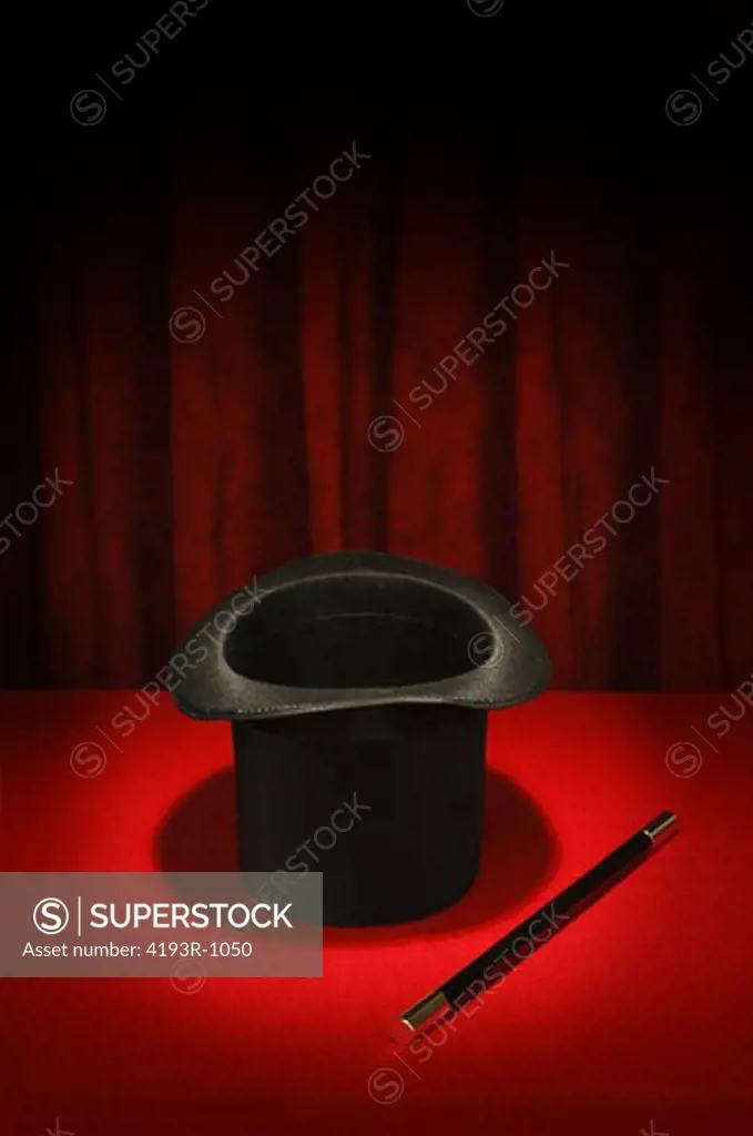 Magician's top hat and magic wand in spotlight on red table cloth and red draped background