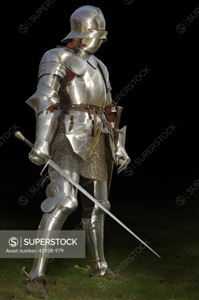 Mediaeval knight in shining armour of the 15th century standing outside with sword. Isolated on a dark background with clipping path