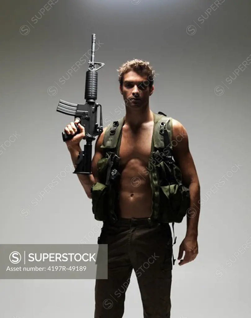 Soldier with a bare chest holding up his M16 rifle while looking seriously at the camera - portrait