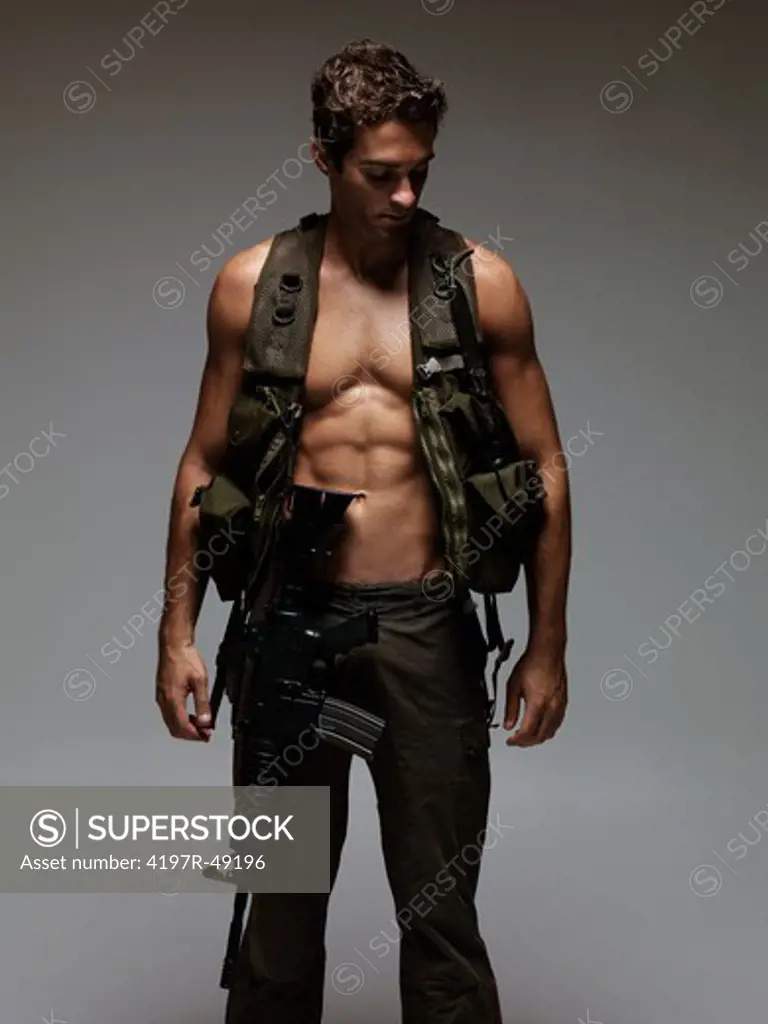 Attractive young soldier revealing a bare chest under his vest glancing downward - isolated