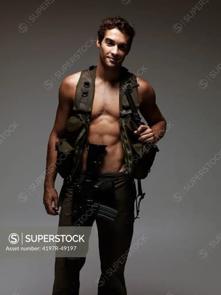 Handsome young soldier smiling at the camera wearing a vest, pants, and a M16 rifle