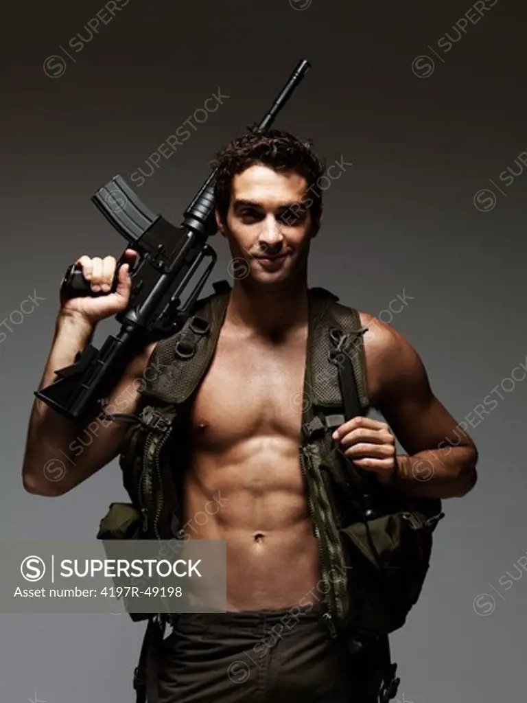 Smiling young man dressed in an army outfit holding up an M16 rifle - portrait