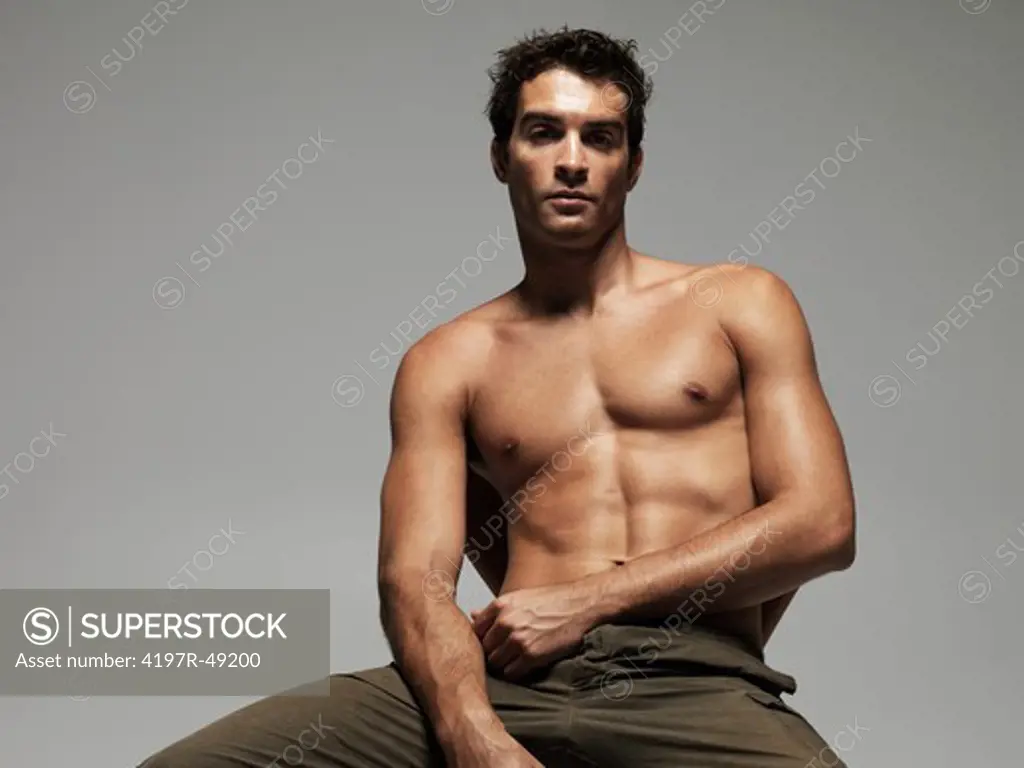 Attractive young man with a bare chest sitting on a chair looking at the camera