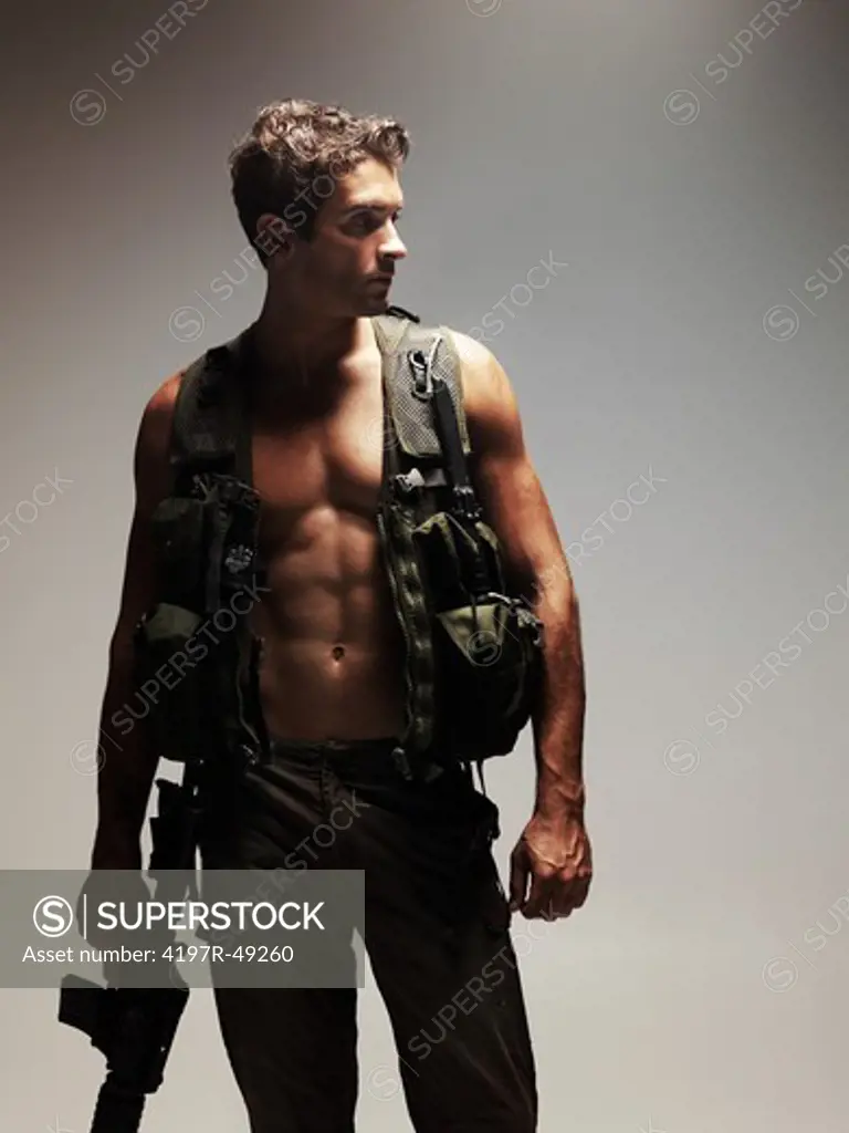Young man holding an M16 rifle dressed in a combat vest and pants looking out of the frame