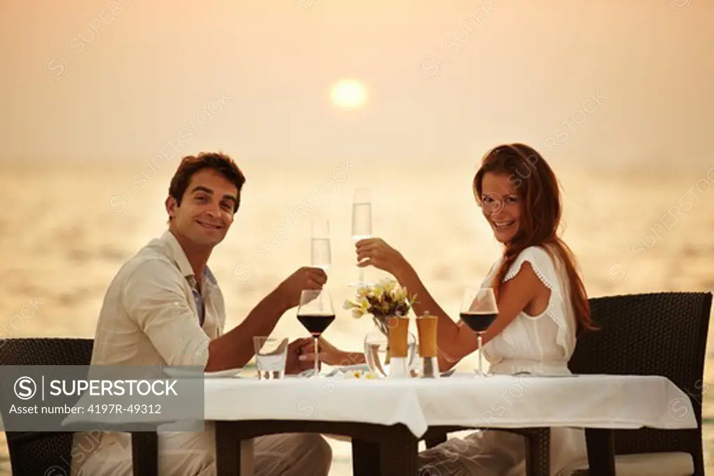 A young couple toast each other while having dinner on the beach in the Maldives