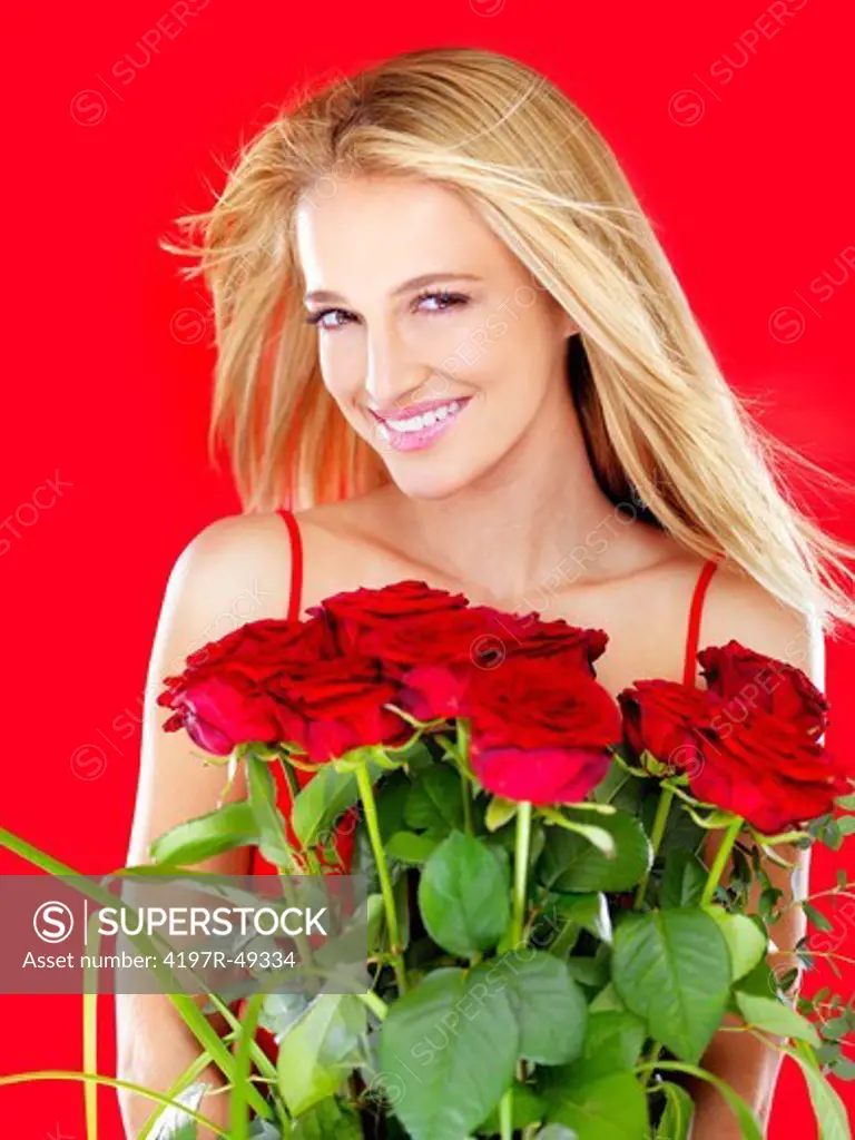 Gorgeous woman smiling while holding a bunch of red roses - isolated on red