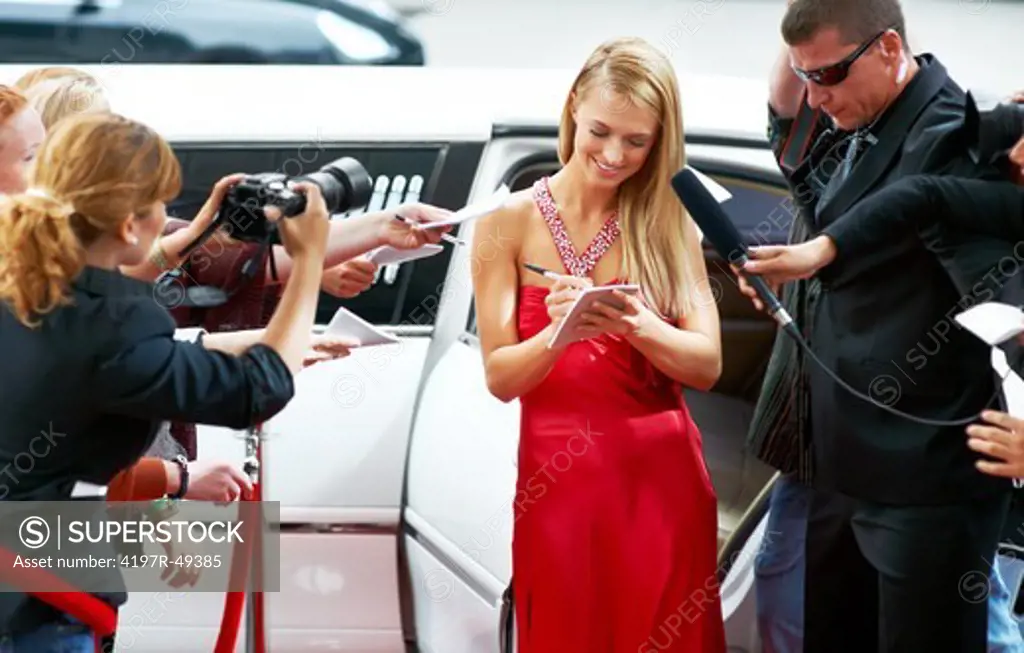 A stunning young actress signing autographs on the red carpet while swamped by paparazzi