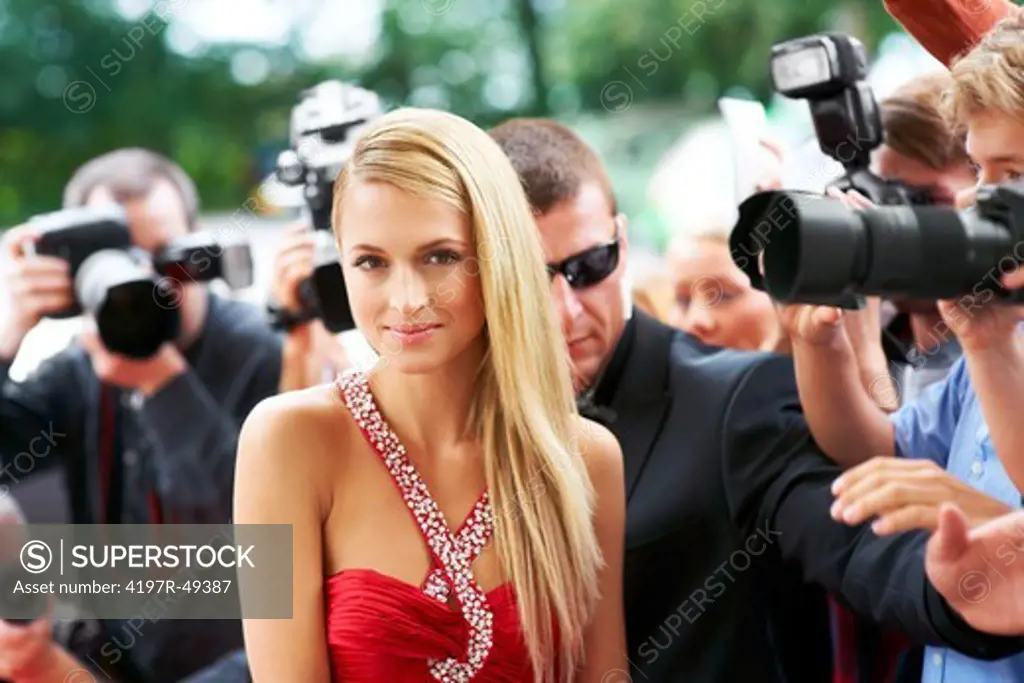 A beautiful actress posing on the red carpet amidst paparazzi and their flashing cameras