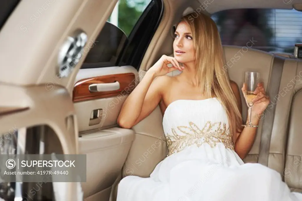 A gorgeous young woman enjoying a glass of champagne while sitting in the luxury of a limousine