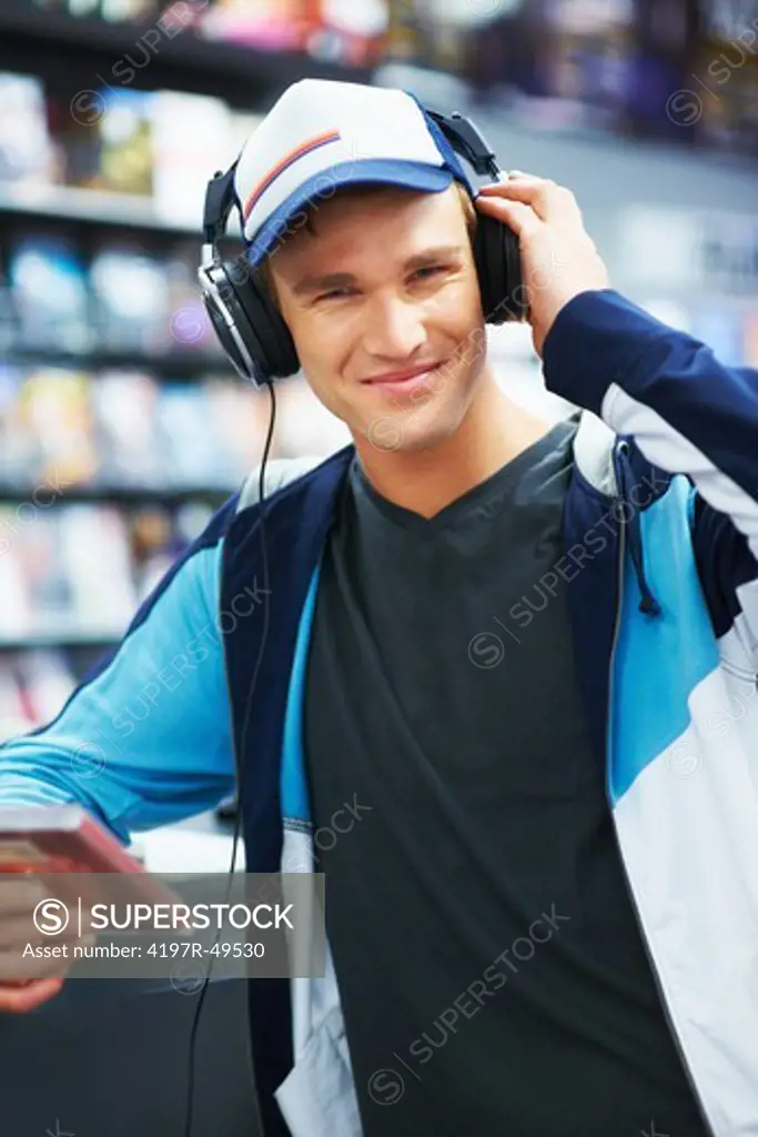 Portrait of a trendy young guy wearing headphones and listening to his favourite band at a music shop