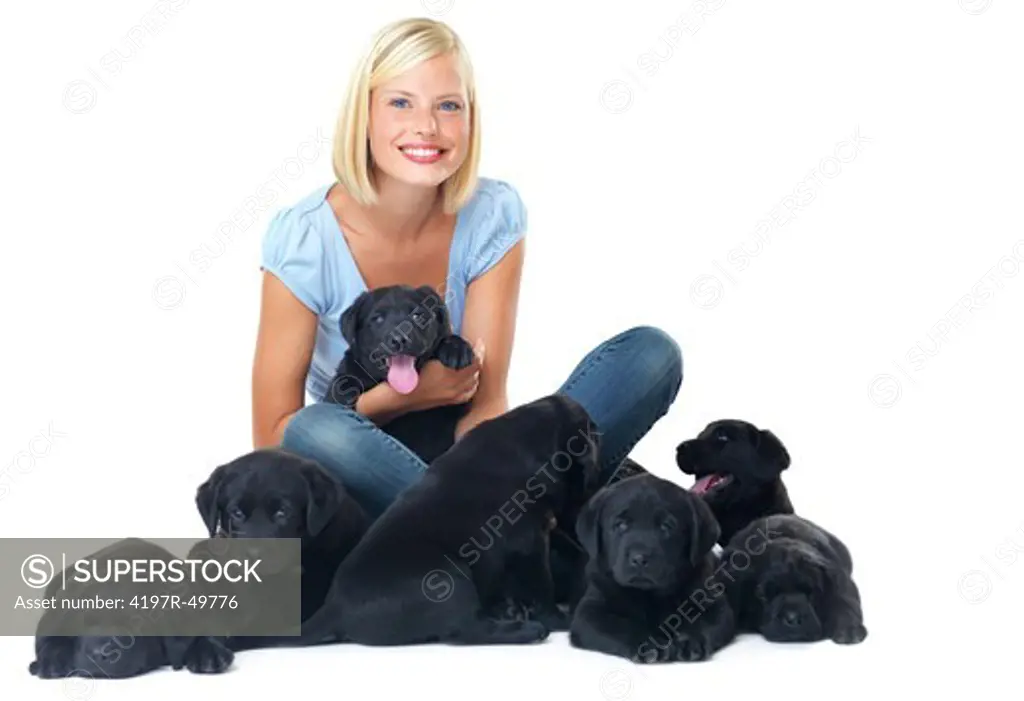 Happy young woman smiling while sitting isolated on white and surrounded by black labrador puppies - portrait