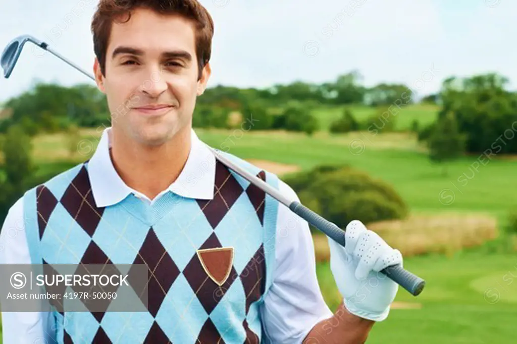 Portrait of a young male golfer holding his club with the golf course in the background