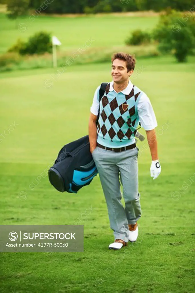 Handsome young golfer carrying his golf bag across the course