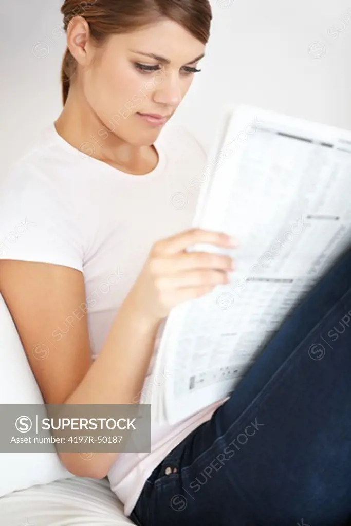 Pretty young female reading the newspaper in the comfort of her own home