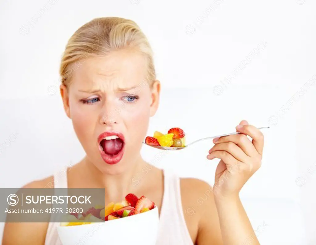 Doubtful young woman eating a fruit salad while isolated on white