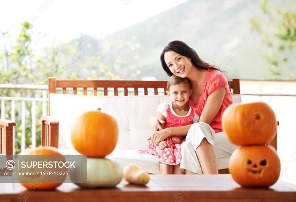 Portrait of a mother and daughter hugging behind a table of pumpkins