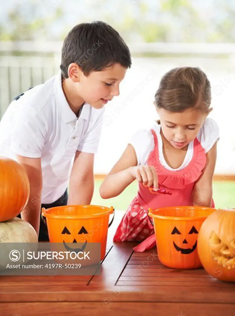 Brother and sister share and look for sweets and chocolate candy in their Halloween baskets of treats