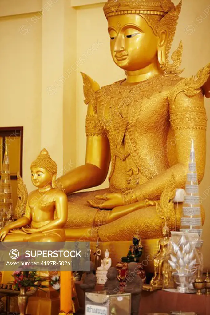 Two golden statues of the Buddha in Thai temple with figurines and offerings