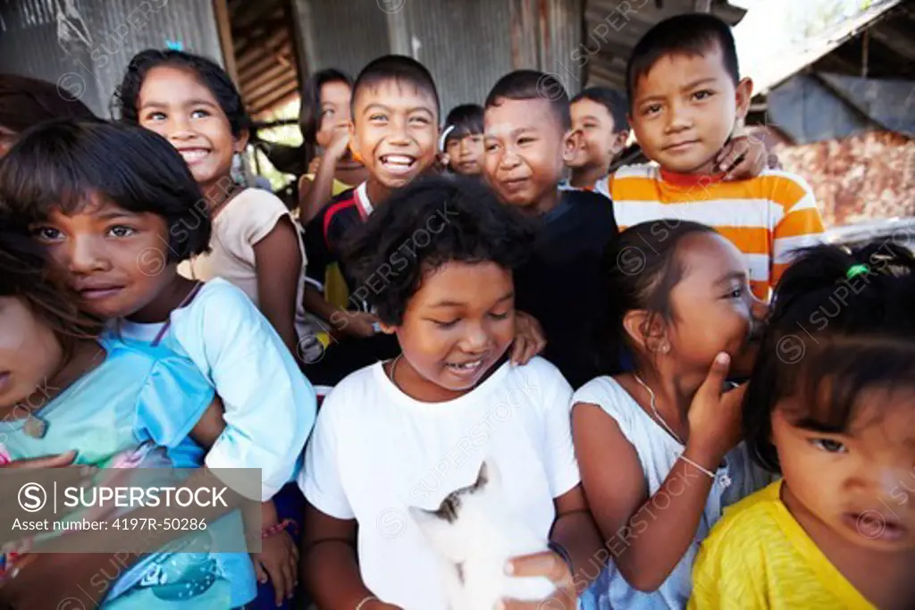 A group of underprivileged children smiling and laughing grouped around a boy holding a kitten