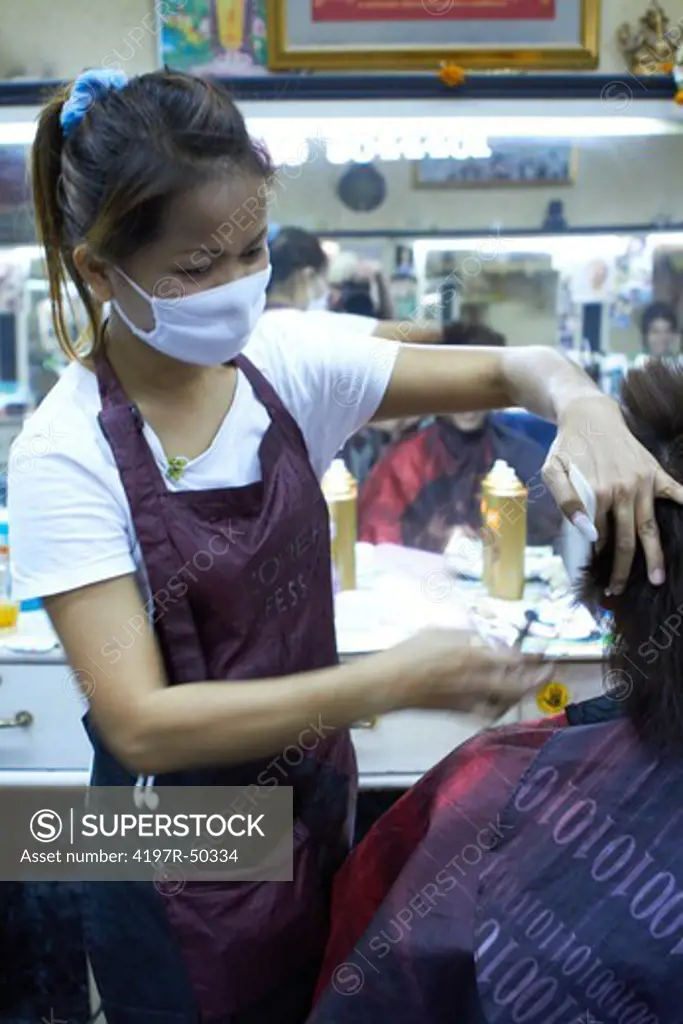 Female Thai hairdresser wearing a surgical mask while cutting hair