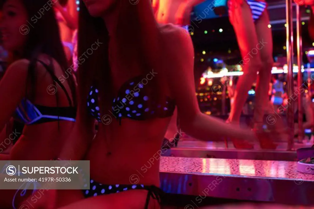 Cropped image of two Thai transgender women in nightclub with poledancers in the background