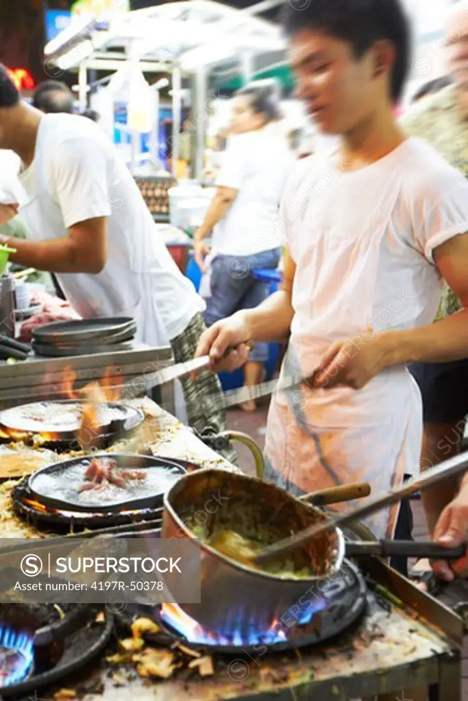 Chefs in a Thai restuarant preparing food on gas stovetops