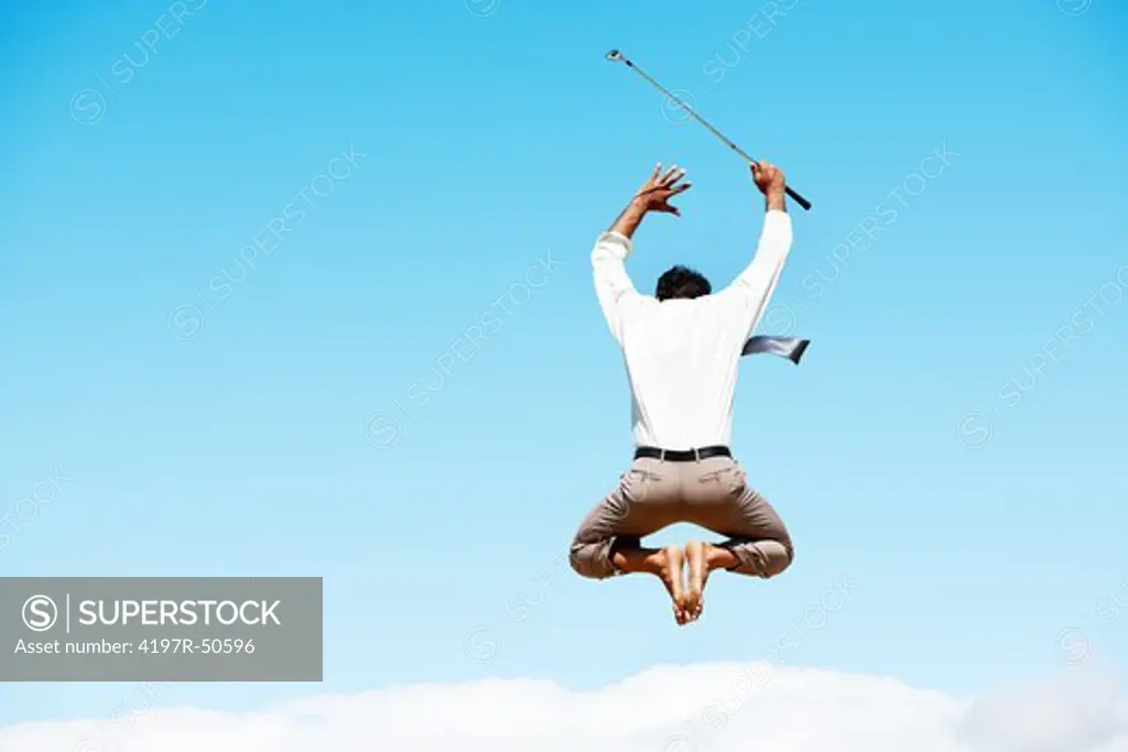 Mature businessman leaping into the air while holding a golf club and wearing no shoes