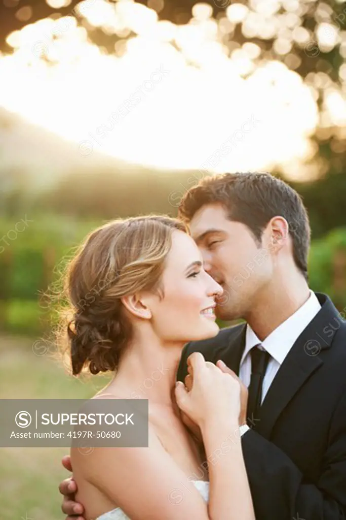Loving groom whispering sweet nothings into his new wife's ear while the sun sets behind them