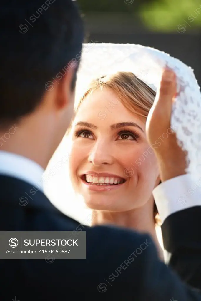 Closeup of a gorgeous bride smiling with happiness as her husband lifts her veil up looking into her eyes