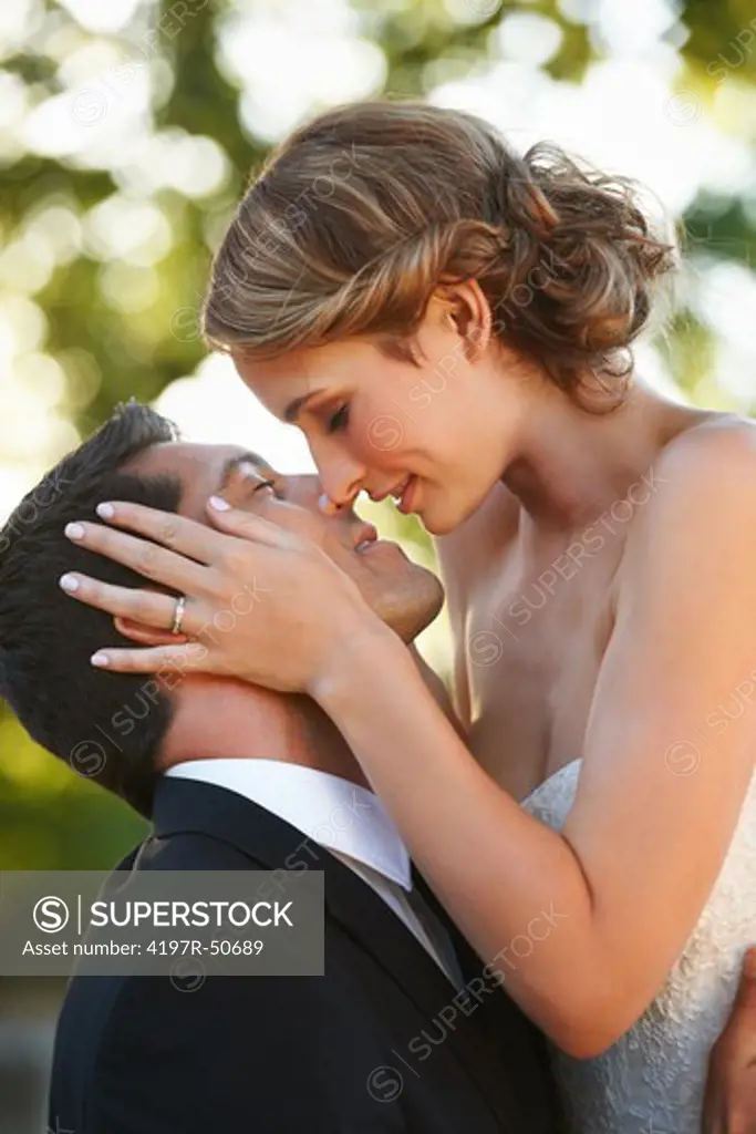 A beautiful bride touches her husband's face as she leans in to kiss him on their wedding day
