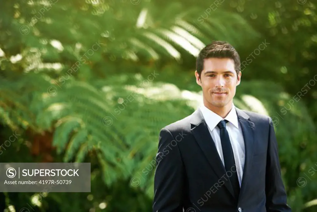 Portrait of a young groom standing wearing a suit in a garden smiling - Copyspace