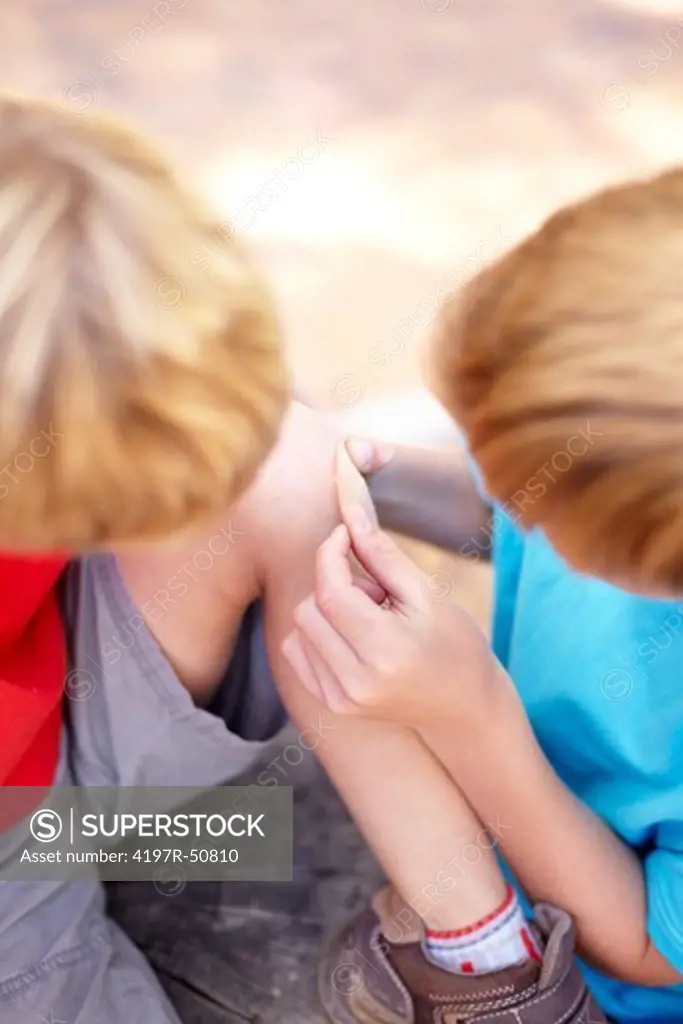 Young boy putting a plaster on his younger brother's knee